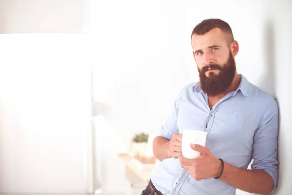 Snygg ung indisk man som innehar kaffekopp och leende samtidigt stående mot vit bakgrund — Stockfoto