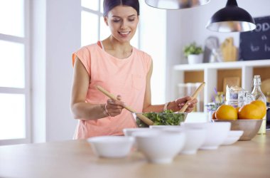 Gülümseyen genç kadın mutfakta taze salata karıştırıyor..