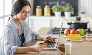 Mutfakta bilgisayar ve kredi kartı kullanan gülümseyen bir kadın.