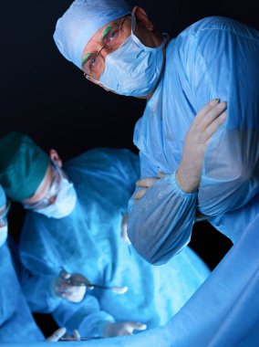 Ameliyathanede çalışan bir grup cerrah mavi tonda çalışıyor. Tıbbi ekip operasyon yapıyor.