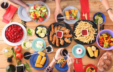 Ahşap masada otururken birlikte yemek yiyen bir grup insanın üst düzey görüntüsü. Masada yemek var. İnsanlar fast food yiyor..