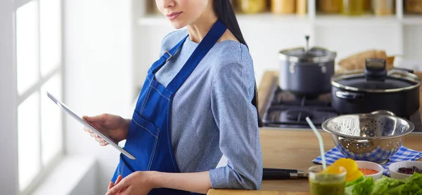 Jovem usando um computador tablet para cozinhar em sua cozinha — Fotografia de Stock