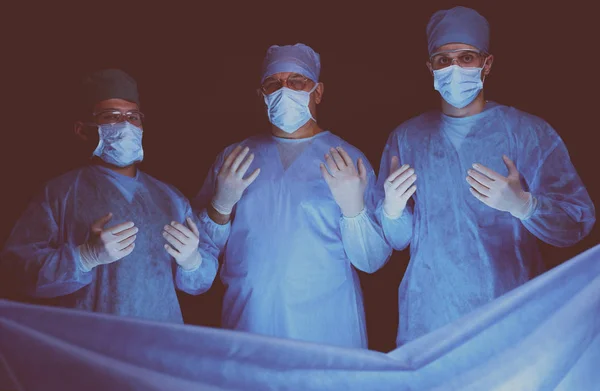 Grupo de cirurgiões no trabalho em sala de operações tonificada em azul. Equipe médica realizando operação — Fotografia de Stock