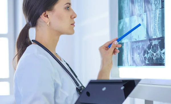 Joven doctora sonriente con estetoscopio apuntando a rayos X en el consultorio médico —  Fotos de Stock