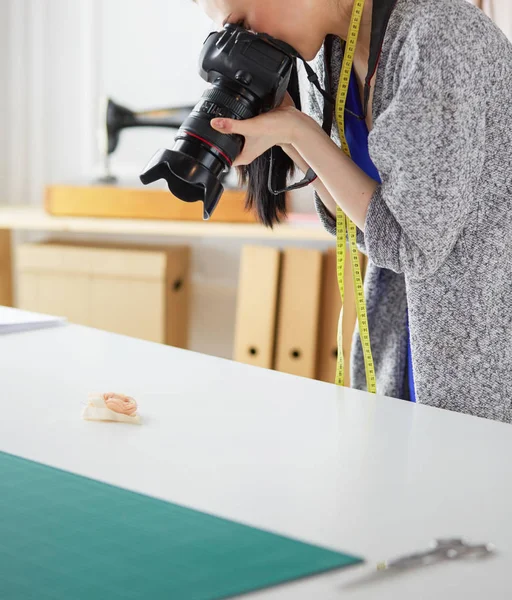 Jonge vrouw ontwerper staat in de buurt van de werkplek en fotograferen op digitale camera — Stockfoto