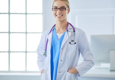 Masanın yanında duran genç doktor kadın, beyaz arka planda soyutlanmış.