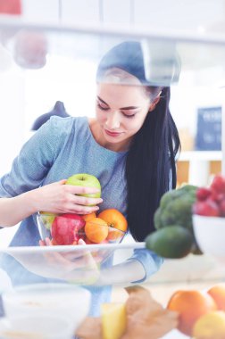 Gülümseyen kadın buzdolabından taze meyve alıyor, sağlıklı yiyecek konsepti.