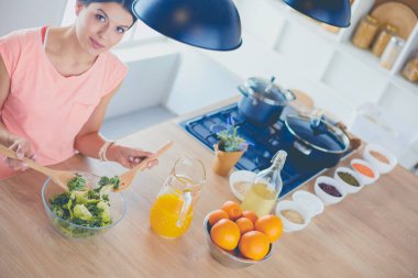 Gülümseyen genç kadın mutfakta taze salata karıştırıyor..