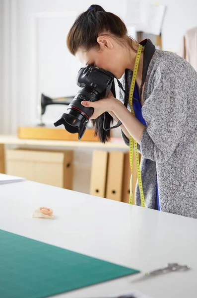 Mujer joven diseñadora de pie cerca del lugar de trabajo y fotografiándolo en una cámara digital — Foto de Stock