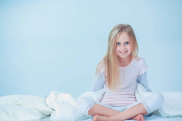 Das kleine Mädchen im Schlafzimmer sitzt auf dem Bett. kleines Mädchen trägt Schlafanzug und sitzt im Bett . — Stockfoto