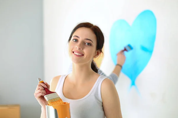 Retrato de feliz casal sorrindo jovem pintura parede interior da nova casa. jovem casal — Fotografia de Stock