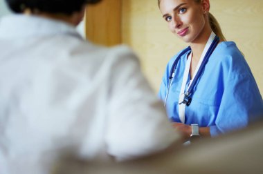 Bir doktor konuşuyor ve bir hastayı muayene ediyor.