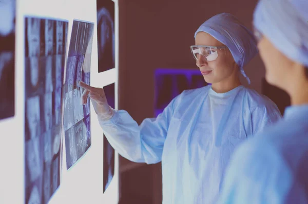 Doctor in hospital sitting at desk looking at x-rays on tablet against white background with x-rays — Stock Photo, Image