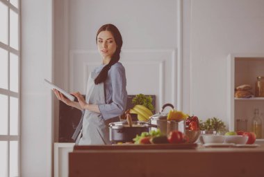 Mutfakta yemek yapmak için tablet bilgisayar kullanan genç bir kadın.