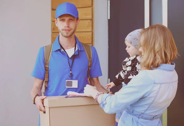 Lächelnder Zusteller in blauer Uniform liefert Paketkasten an Empfänger aus - Kurierdienst-Konzept. Lächelnder Zusteller in blauer Uniform — Stockfoto