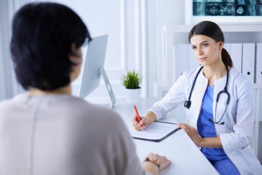 Doktor ve hasta hastane danışma odasında tıbbi sorunları tartışıyorlar. Doktor hasta formunu dolduruyor.