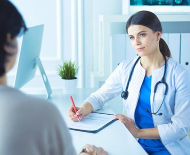 Doktor ve hasta hastane danışma odasında tıbbi sorunları tartışıyorlar. Doktor hasta formunu dolduruyor.