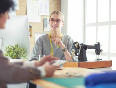 Yeni moda tarzlar yaratıyor. Moda atölyesinde çalışırken dikiş diken neşeli genç bir kadın.