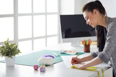 Moda tasarımcıları stüdyoda çalışıyor, masanın yanında duruyorlar.