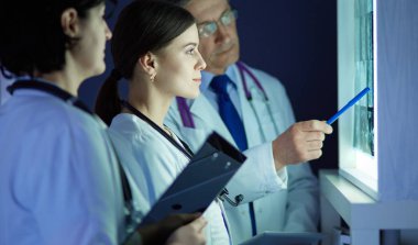 Bir grup doktor bir klinikte röntgenleri inceliyor, teşhis koymayı düşünüyorlar.