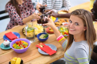 Ahşap masada otururken birlikte yemek yiyen bir grup insanın üst düzey görüntüsü. Masada yemek var. İnsanlar fast food yiyor. Bir kızın portresi.