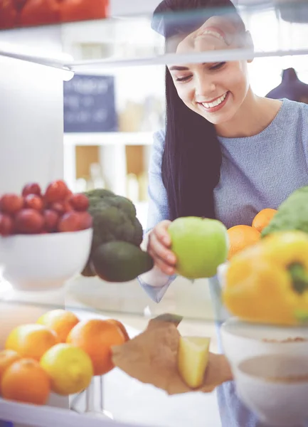 Smiling woman taking a fresh fruit out of the fridge, healthy food concept — Stock Photo, Image