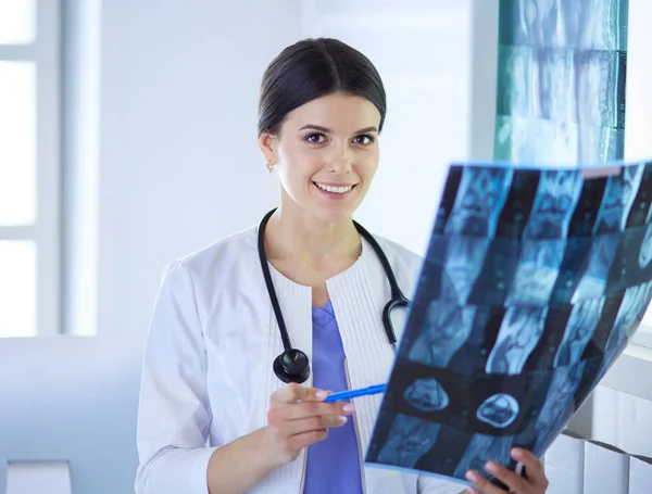 Νεαρή χαμογελαστή γυναίκα γιατρός με στηθοσκόπιο που κοιτάζει ακτινογραφία στο ιατρείο — Φωτογραφία Αρχείου