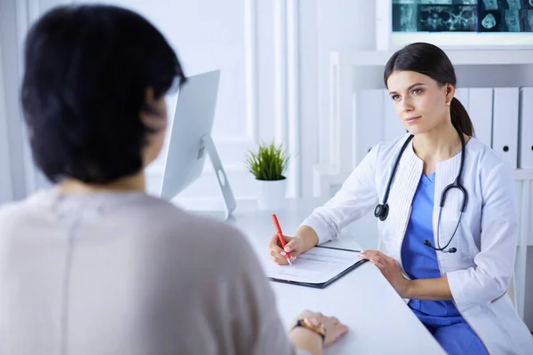 Médico y paciente discutiendo problemas médicos en una sala de consulta del hospital. Doc rellenando un formulario de pacientes — Foto de Stock