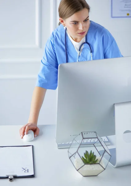 Portrait of female physician filling up medical form while standing near reception desk at clinic or emergency hospital