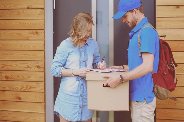 Mavi üniformalı gülümseyen kurye servis konseptine paket kutusu teslim eden teslimatçı. Mavi üniformalı gülümseyen teslimatçı.