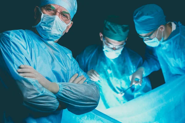 Gruppe von Chirurgen bei der Arbeit in einem blau getönten Operationssaal. Medizinisches Team bei der Operation — Stockfoto