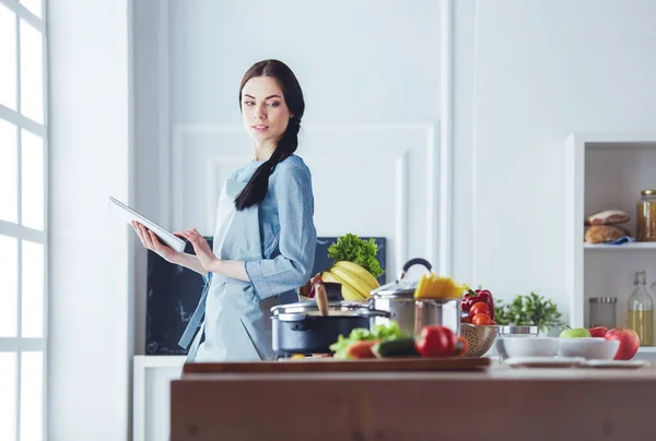 Young woman using a tablet computer to cook in her kitchen — Stock Photo, Image