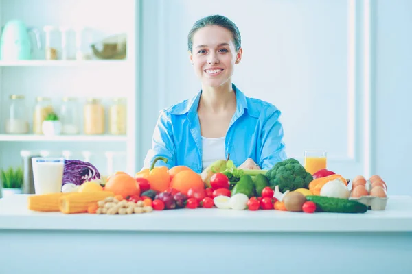 Mujer joven y linda sentada en la mesa llena de frutas y verduras en el interior de madera. — Foto de Stock