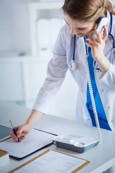 Jovem médico praticante que trabalha na recepção da clínica, ela está atendendo telefonemas e agendando consultas — Fotografia de Stock