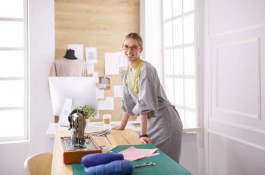 Yeni moda tarzlar yaratıyor. Moda atölyesinde çalışırken dikiş diken neşeli genç bir kadın.