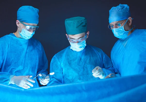 Grupo de cirurgiões no trabalho em sala de operações tonificada em azul. Equipe médica realizando operação — Fotografia de Stock