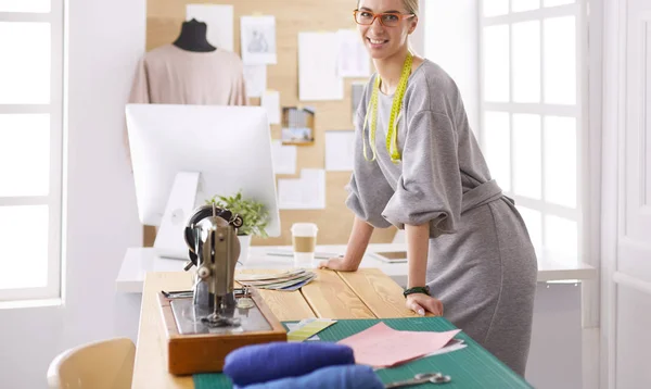Neue modische Stile schaffen. Fröhliche junge Frau näht, während sie an ihrem Arbeitsplatz in der Modewerkstatt sitzt — Stockfoto