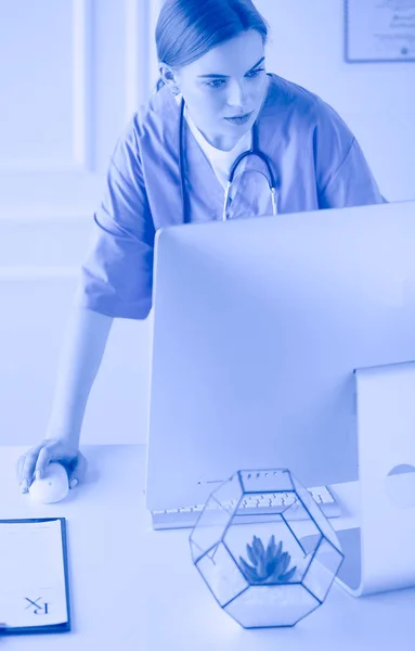 Portrait of female physician filling up medical form while standing near reception desk at clinic or emergency hospital