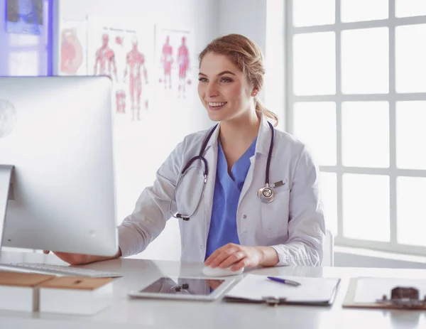 Jonge vrouwelijke arts zit aan een bureau en werkt aan de computer in het ziekenhuiskantoor. Gezondheidszorg, verzekeringen en hulp concept. Artsen klaar om de patiënt te onderzoeken — Stockfoto