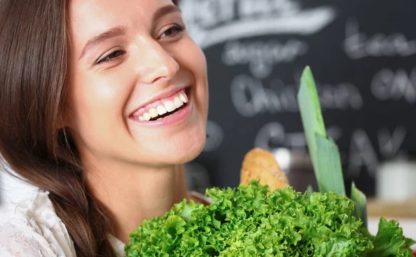 Mujer joven sonriente sosteniendo verduras de pie en la cocina. Jovencita sonriente —  Fotos de Stock