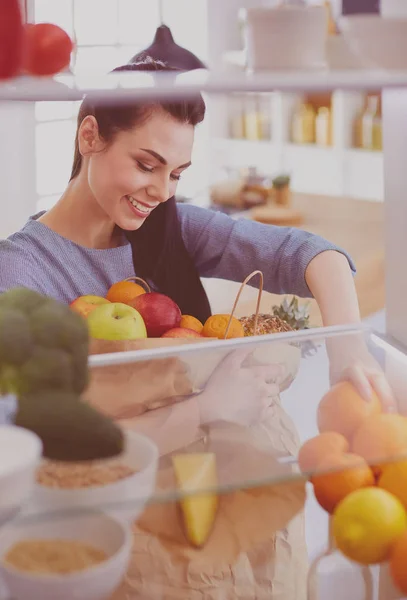 Mulher sorridente tirando uma fruta fresca da geladeira, conceito de comida saudável — Fotografia de Stock