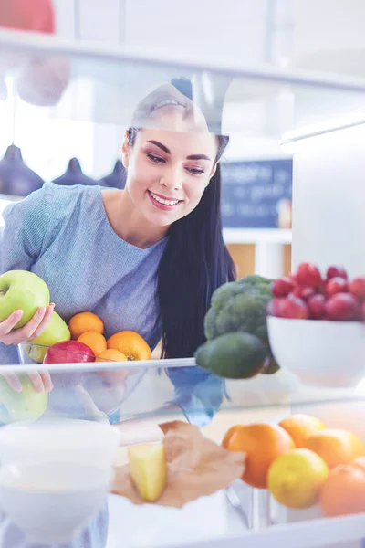 Smiling woman taking a fresh fruit out of the fridge, healthy food concept — Stock Photo, Image