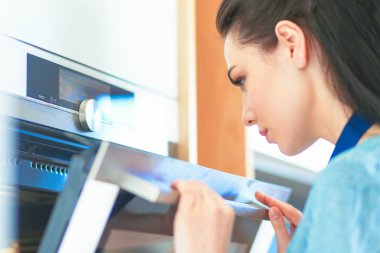 Güzel genç bayan pastasının fırında ne yaptığını kontrol ediyor.