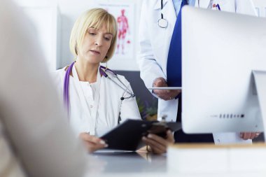 Kadın doktor dizüstü bilgisayarla masada oturuyor, çalışıyor.