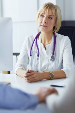 Kadın doktor masada oturuyor ve hastanede dizüstü bilgisayarla çalışıyor.