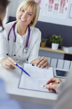 Doktor ve hasta tıbbi kayıtları olan bir dosyayı inceliyor. Tekerlekli sandalyede oturuyor.