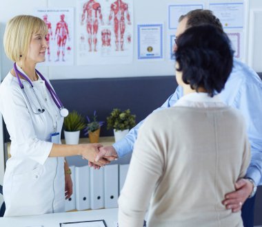 Kadın doktor bir hastanın elini sıkıyor ve gülümsüyor.