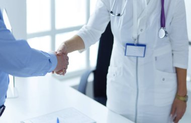 Kadın doktor bir hastanın elini sıkıyor ve gülümsüyor.