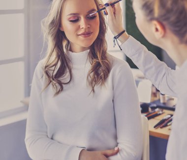 Makyaj sanatçısı genç ve güzel gelinin makyajını yapıyor.