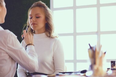 Makyöz, genç bir kadının profesyonel makyajını yapıyor.